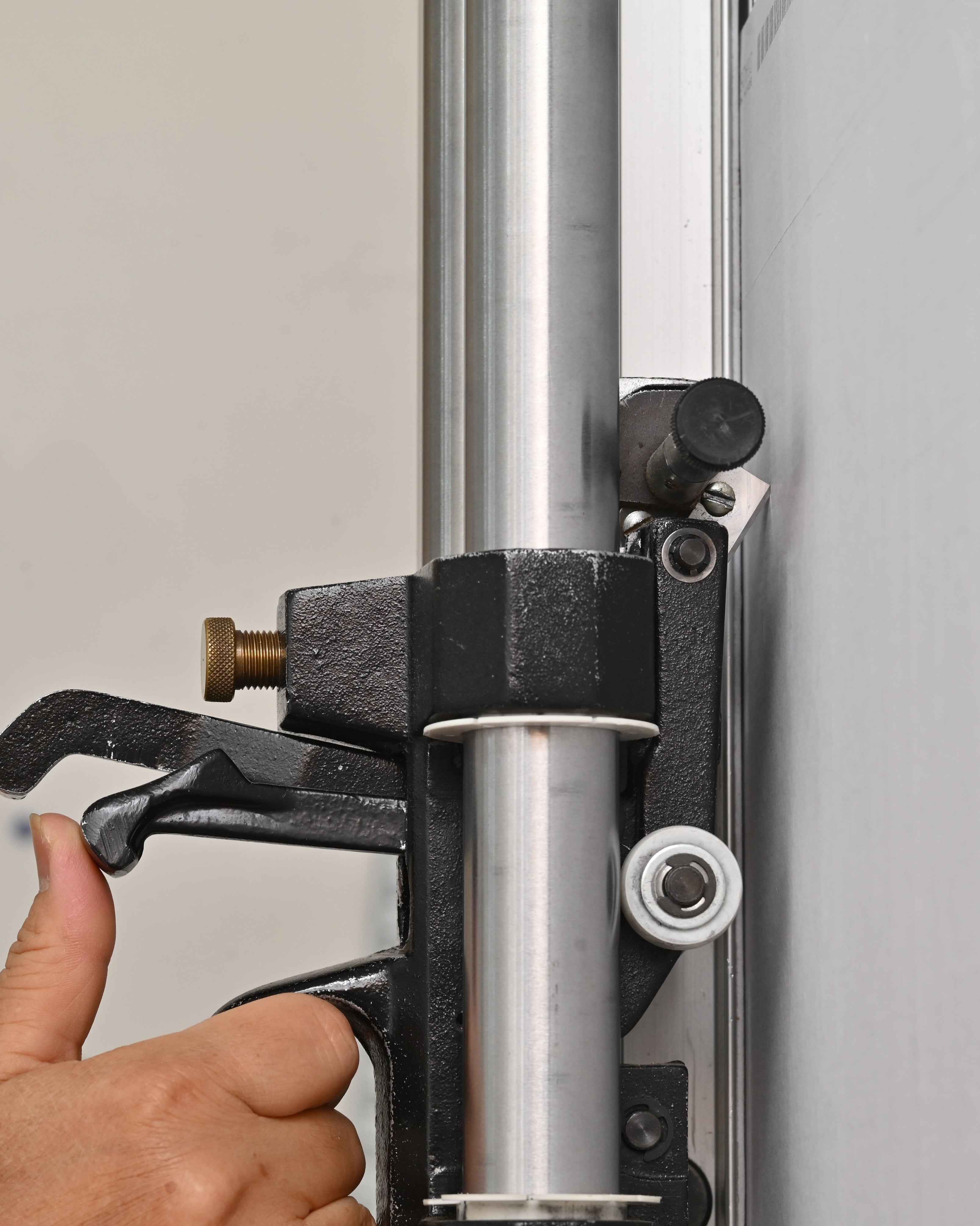 A close-up of a hand operating a black lever clamp attached to a vertical metal pole on a light gray panel.